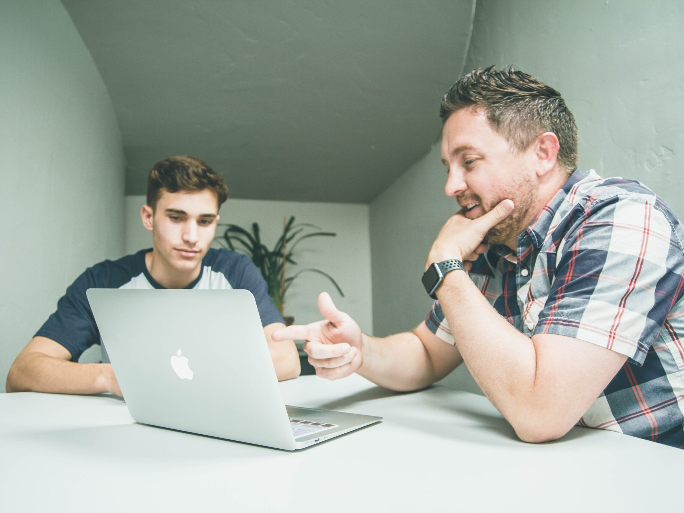 man wearing white and black plaid button-up sports shirt pointing the silver MacBook