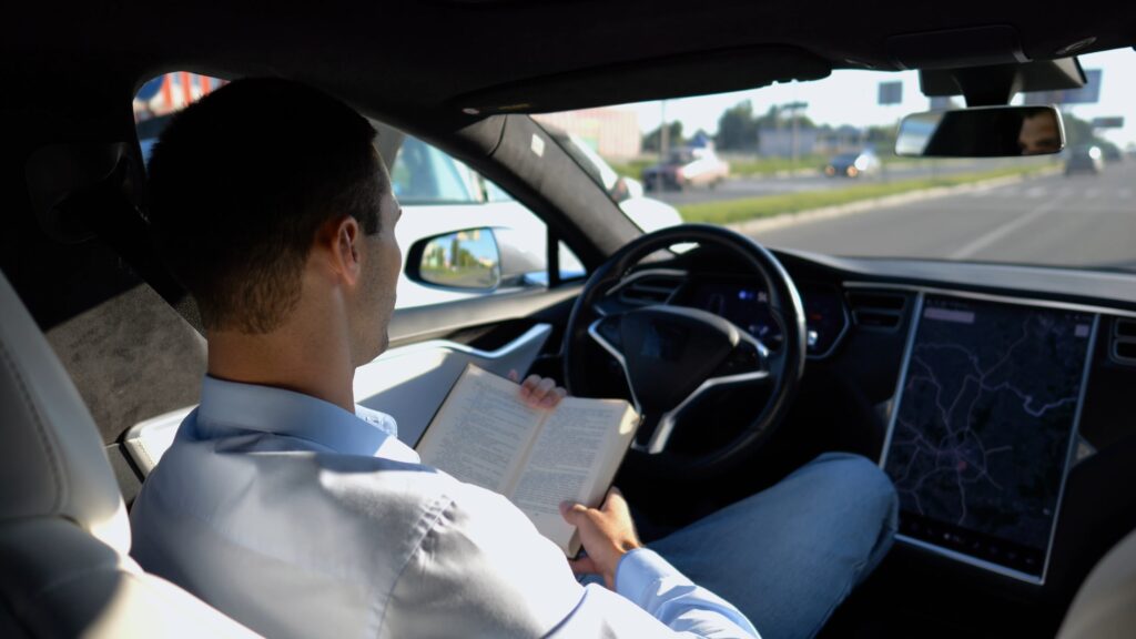Muž sed&iacute; za volantem a m&iacute;sto ř&iacute;zen&iacute; si čte kn&iacute;žku