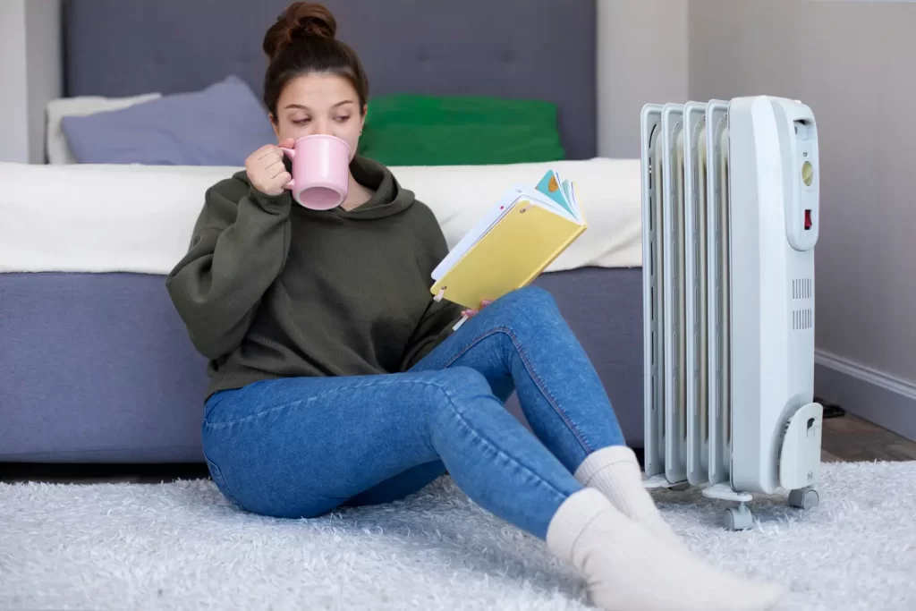 Žena čte, pije a ohřívá se u přenosného topidla.