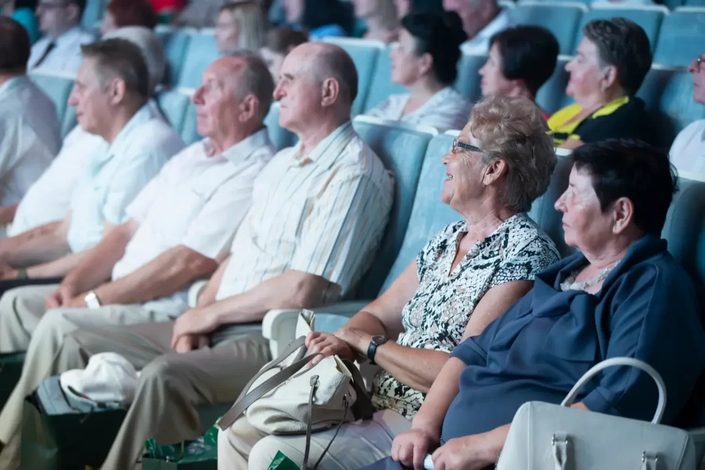 Senioři sed&iacute; v kině.