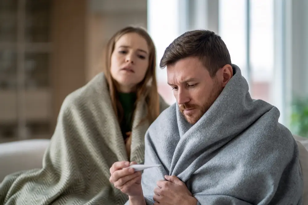 Muž a žena sedí na gauči a měří si teplotu.