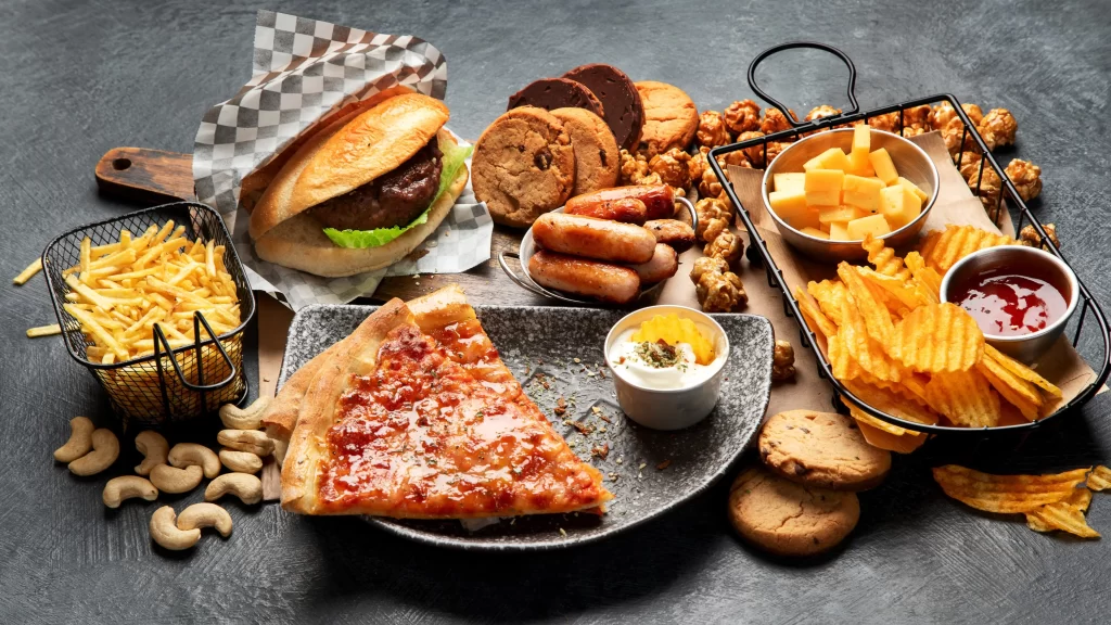 Tučné jídlo jako pizza, hranolky a burger na stole.