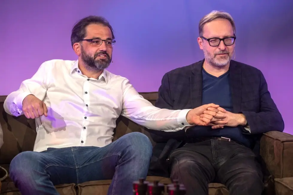 Dva muži v košilích sedící na gauči. 