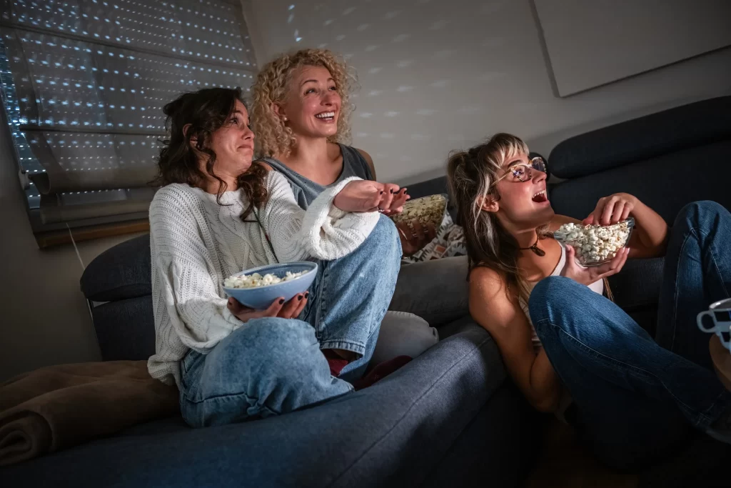 3 ženy s popcornem dívající se na televizi. 