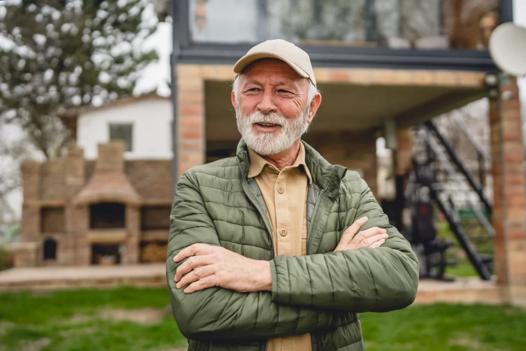 Starší muž stojící před domem se zahradou. 