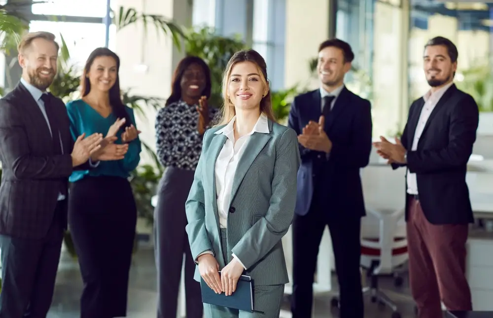 Pět lid&iacute; tlesk&aacute; ženě, kter&aacute; se usm&iacute;v&aacute; na kameru. 