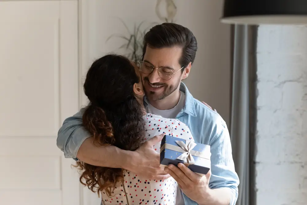 Muž drž&iacute; d&aacute;rek a obj&iacute;m&aacute; ženu. 