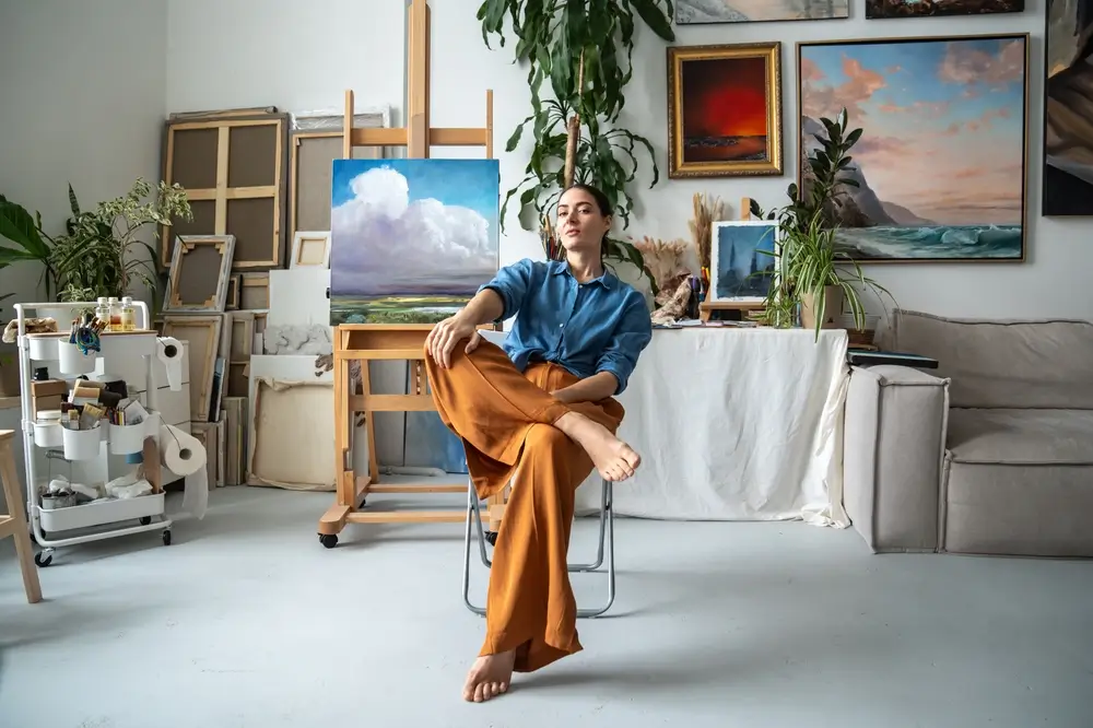 Žena sed&iacute; v pokoji pln&eacute;m obrazů. 