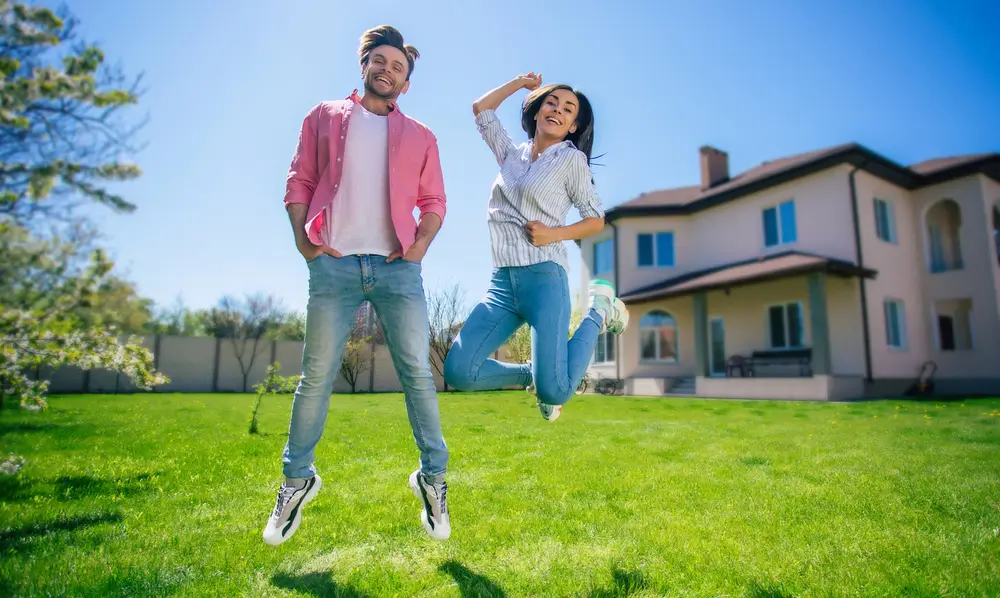 Žena skáče spolu s mužem před velkým barákem.