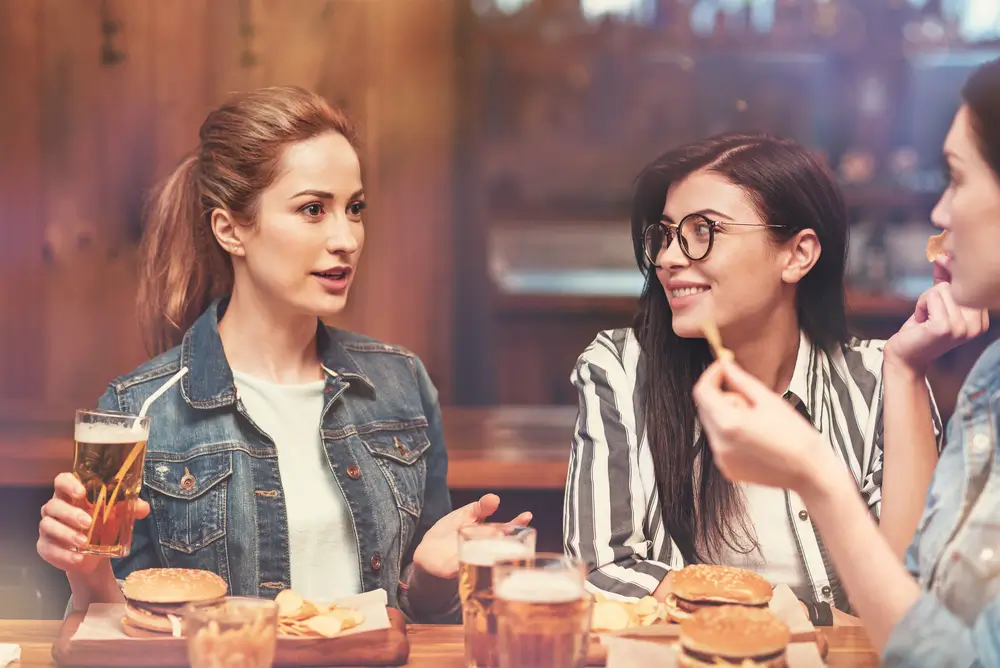 Ženy u stolu s hamburgery a drinky. 