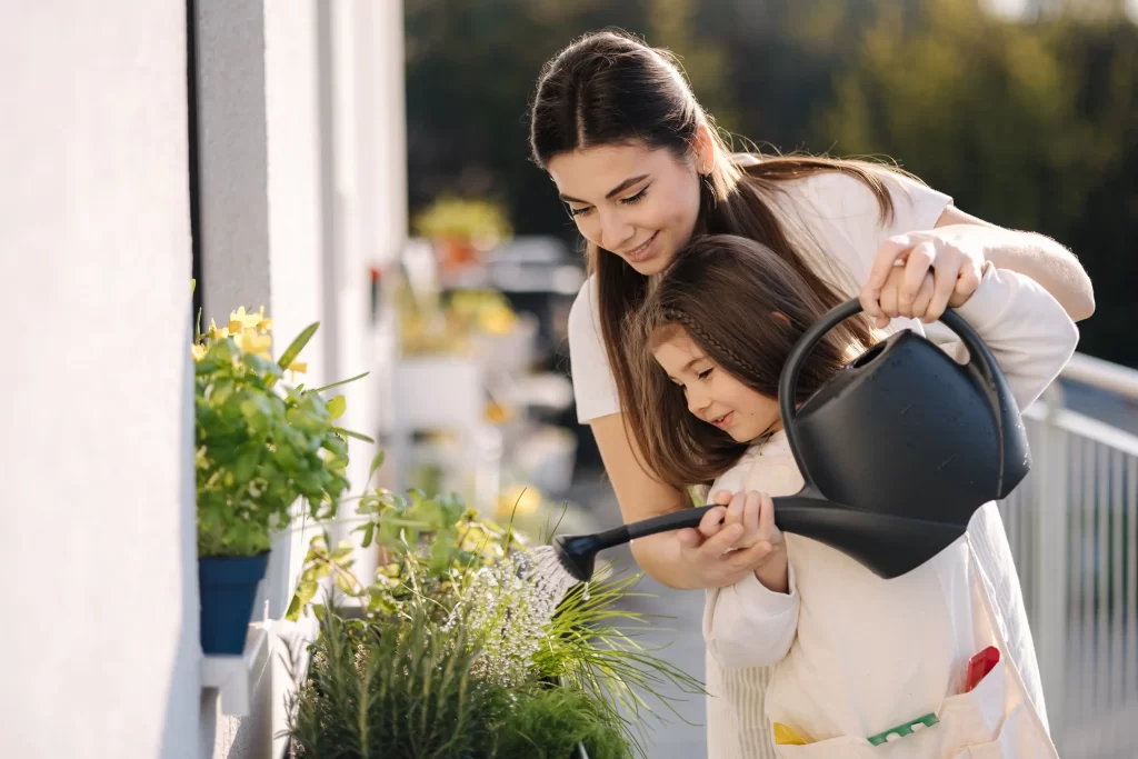 Matka s dcerou zal&eacute;vaj&iacute;c&iacute; květiny na balkoně.