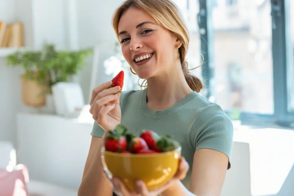 Mladá žena drží v ruce misku plnou jahod.