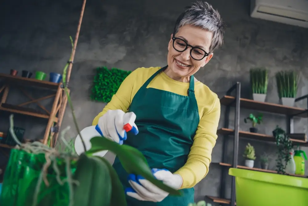 Žena stř&iacute;k&aacute; vodu na květinu pomoc&iacute; rozpra&scaron;ovače. 