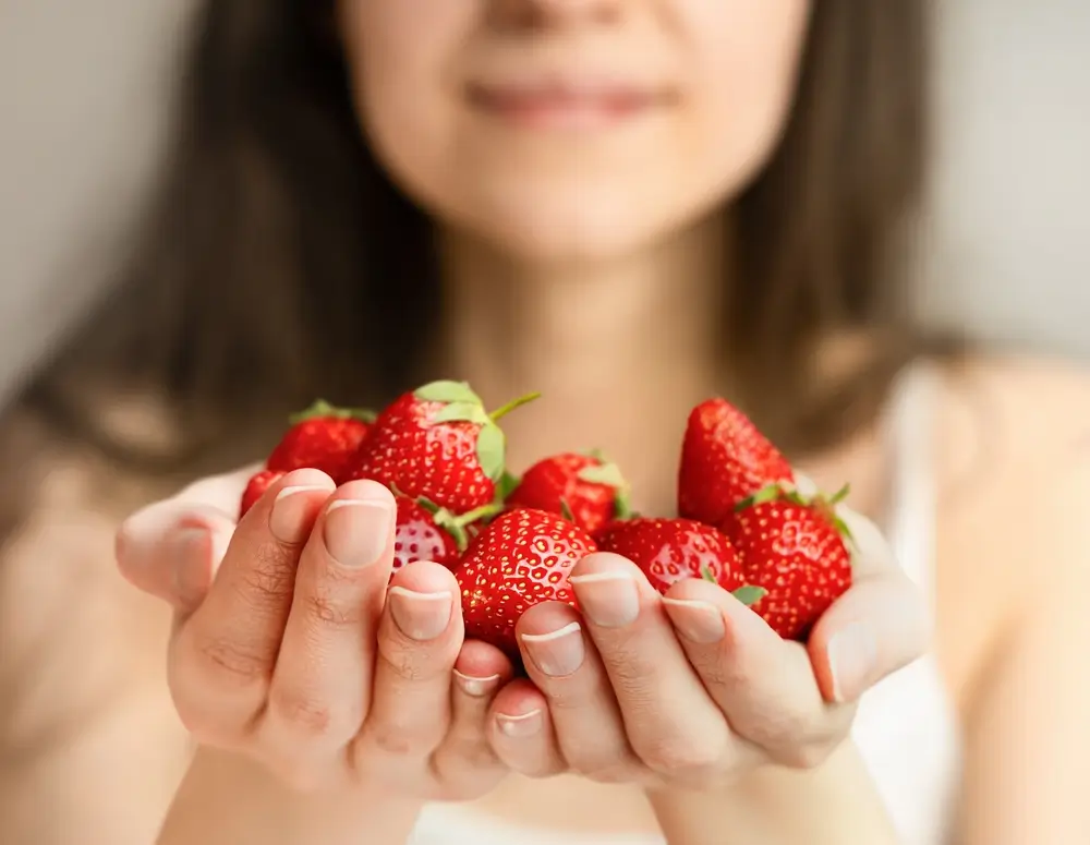 Žena drží v dlaních jahody.