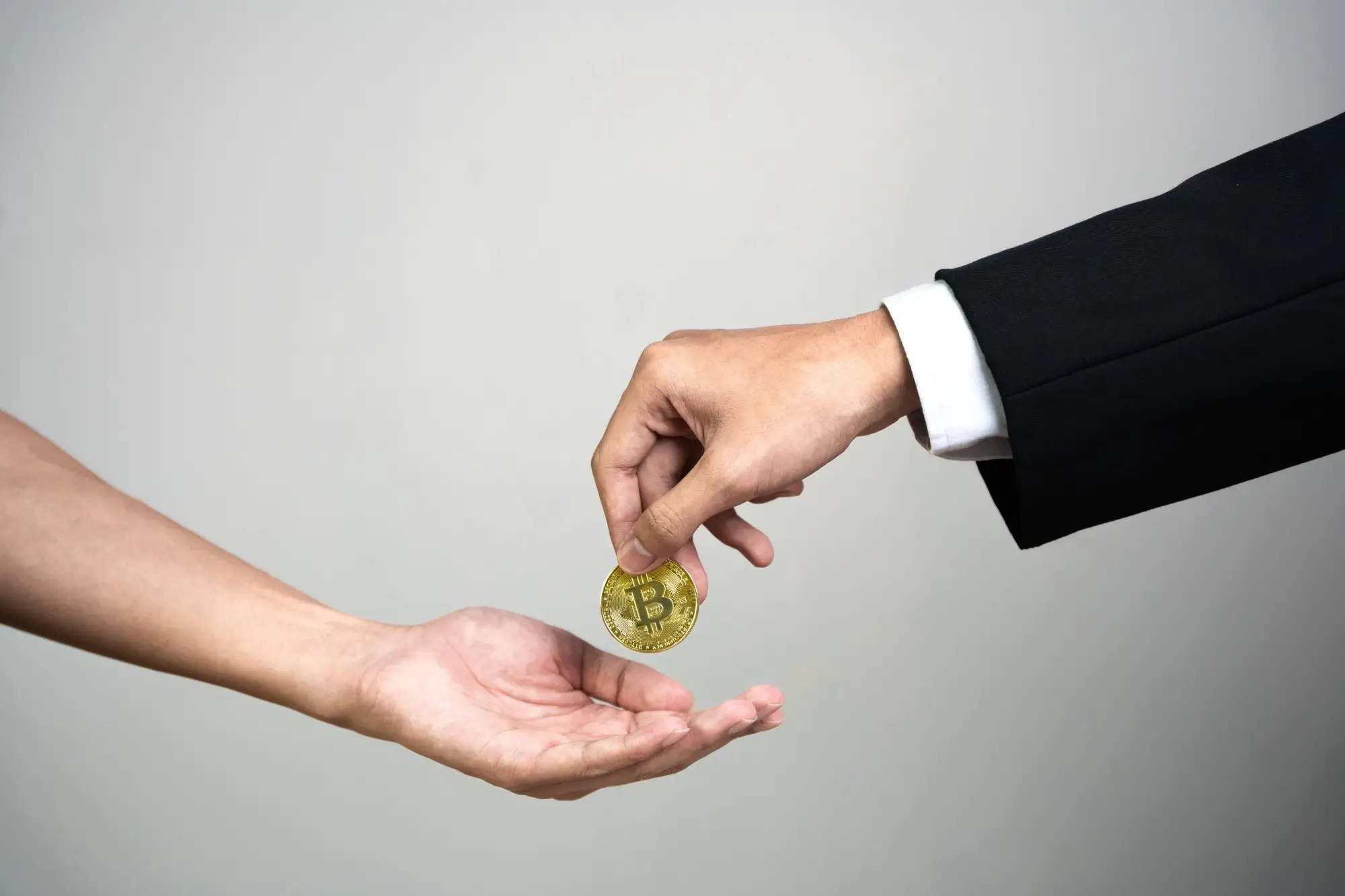 Dvě lidské ruce podávající si zlatou minci.