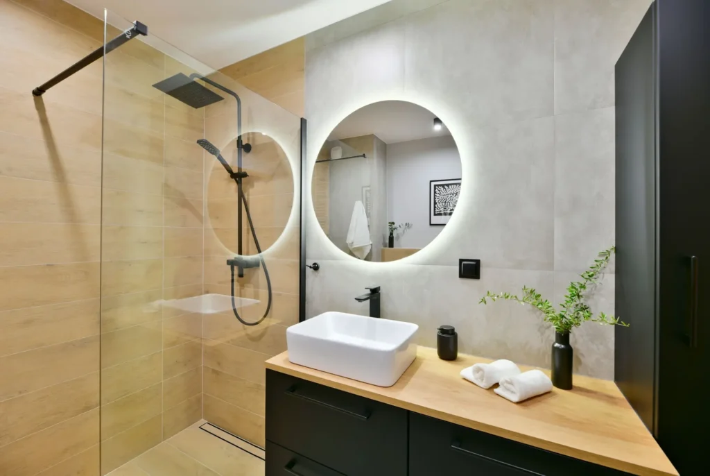 Modern&iacute; koupelna se sprchov&yacute;m koutem a kulat&yacute;m zrcadlem s LED podsv&iacute;cen&iacute;m