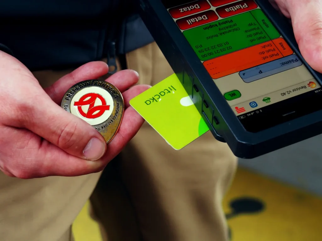 Detailn&iacute; z&aacute;běr na ruku revizora, kter&yacute; drž&iacute; identifikačn&iacute; odznak a kontroln&iacute; zař&iacute;zen&iacute;.