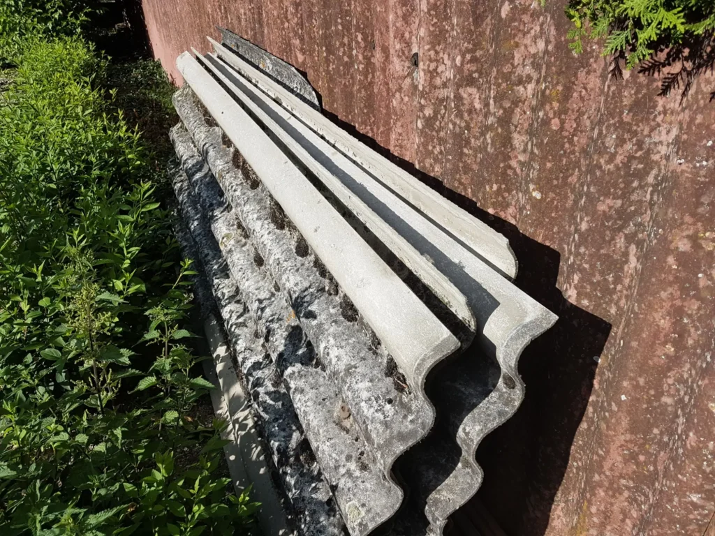 Složen&eacute; star&eacute; vlnit&eacute; desky z eternitu opřen&eacute; o zeď, jejich povrch je již poru&scaron;en&yacute; a zneči&scaron;těn&yacute;.