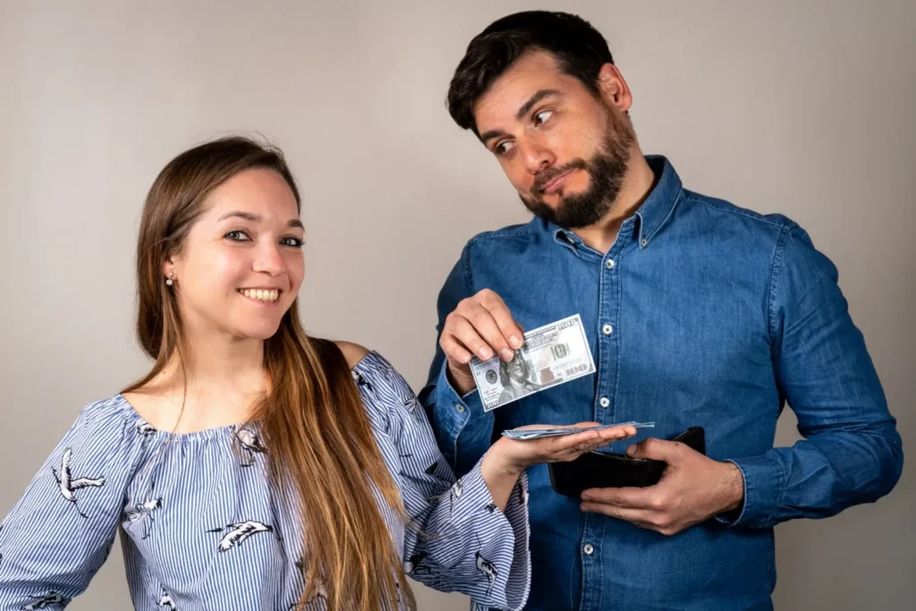 Usměvav&aacute; žena dost&aacute;v&aacute; pen&iacute;ze od muže, kter&yacute; v&aacute;h&aacute; s otevřenou peněženkou