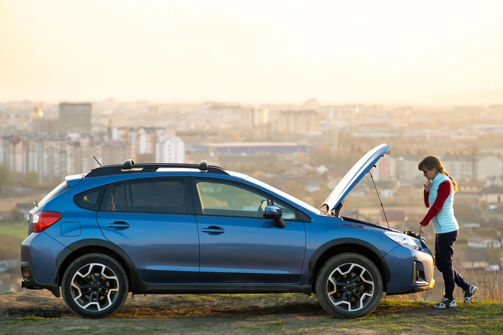 Mladá žena hledící pod kapotu vozu.