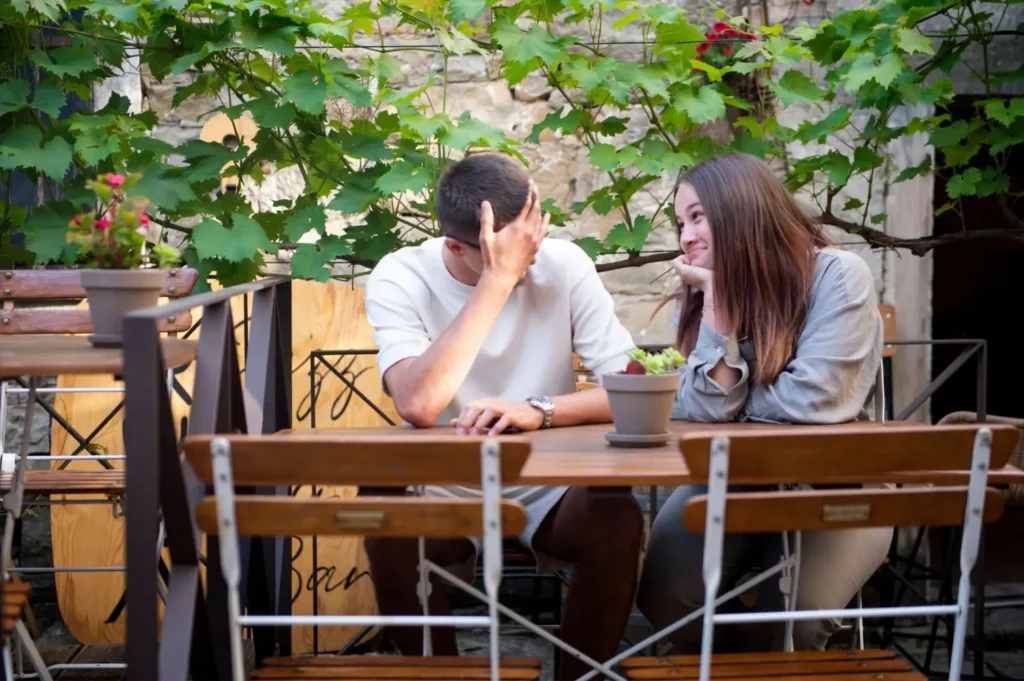 Dva lid&eacute; si pov&iacute;daj&iacute; a směj&iacute; se u stolku na venkovn&iacute; kav&aacute;rensk&eacute; zahr&aacute;dce