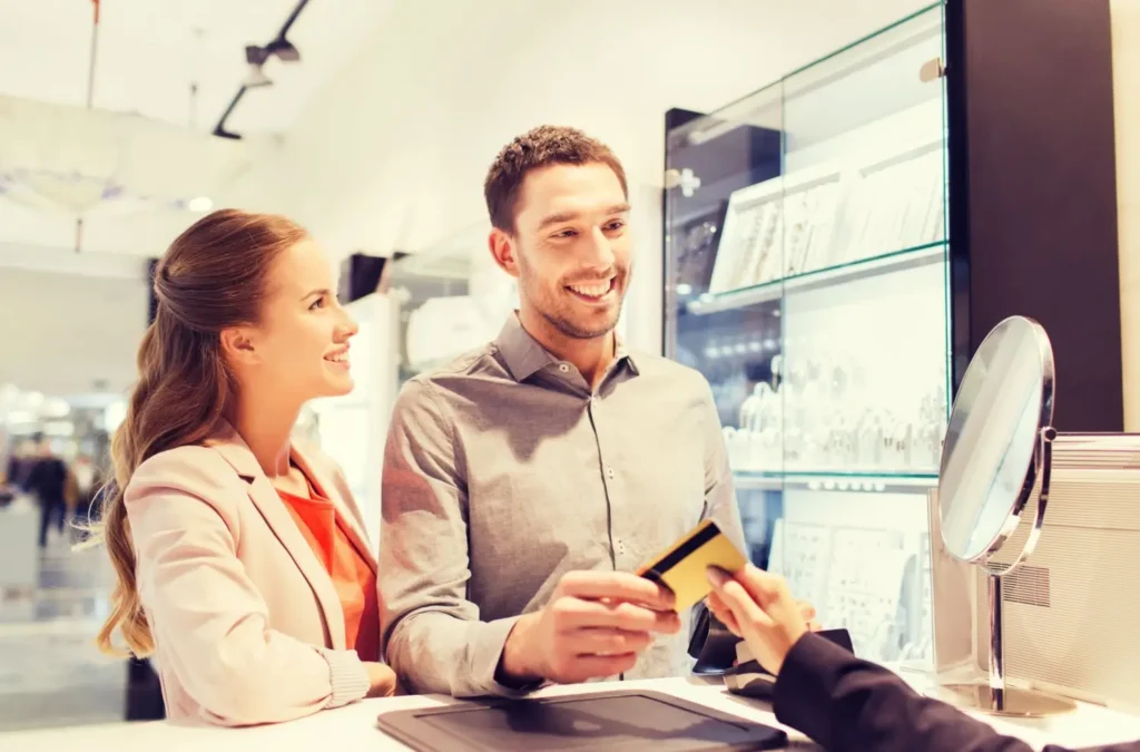 Usměvav&yacute; muž plat&iacute; kartou v obchodě, zat&iacute;mco vedle něj stoj&iacute; spokojen&aacute; partnerka