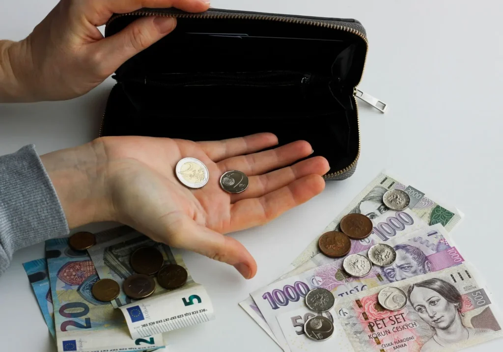 Ruka drží mince, na stole rozložené české koruny a eura