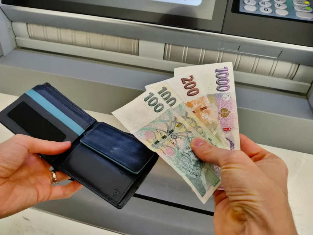 Ruce ukládající české bankovky do peněženky před bankomatem