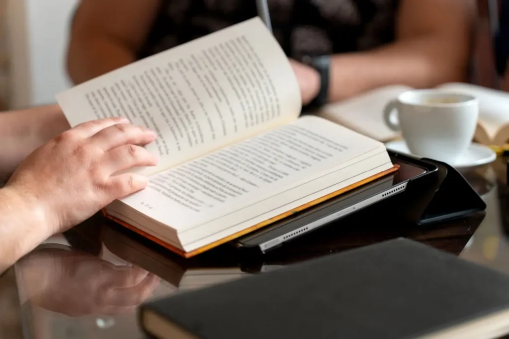 Detailní pohled na otevřenou knihu při čtení u stolu s šálkem kávy