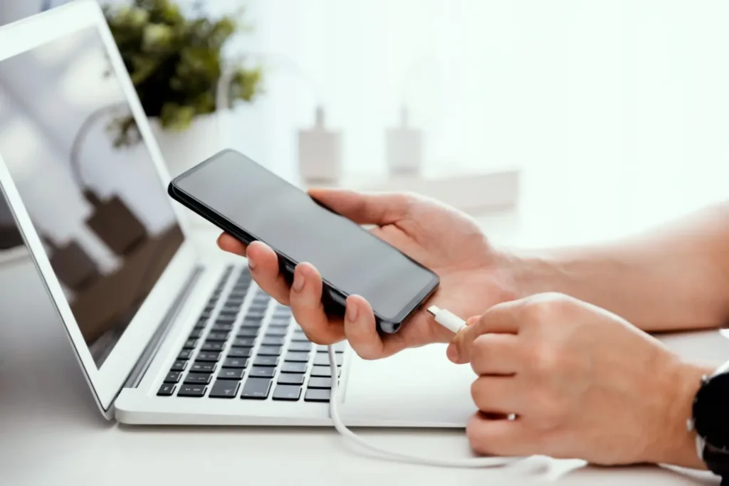 Muž připojuje chytr&yacute; telefon k notebooku pomoc&iacute; nab&iacute;jec&iacute;ho kabelu