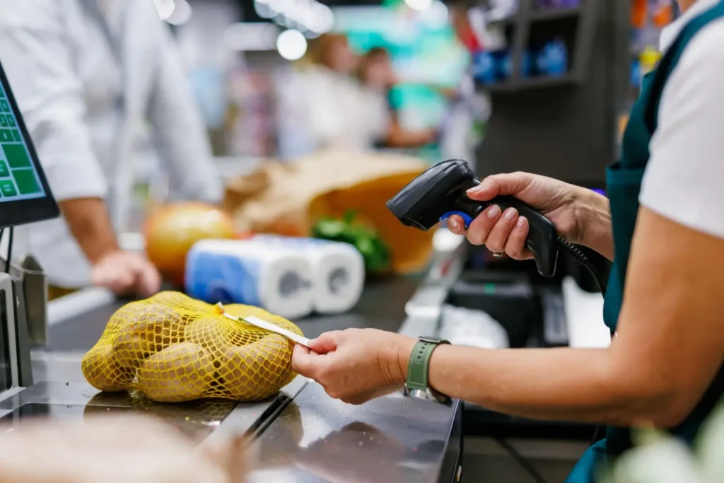 Detail ruky pokladní, která pomocí čtečky skenuje brambory v síťce na pokladním pásu