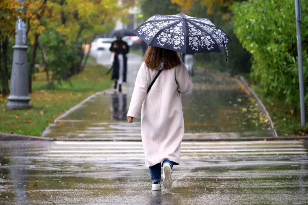 Žena v kabátu jde s deštníkem po ulici