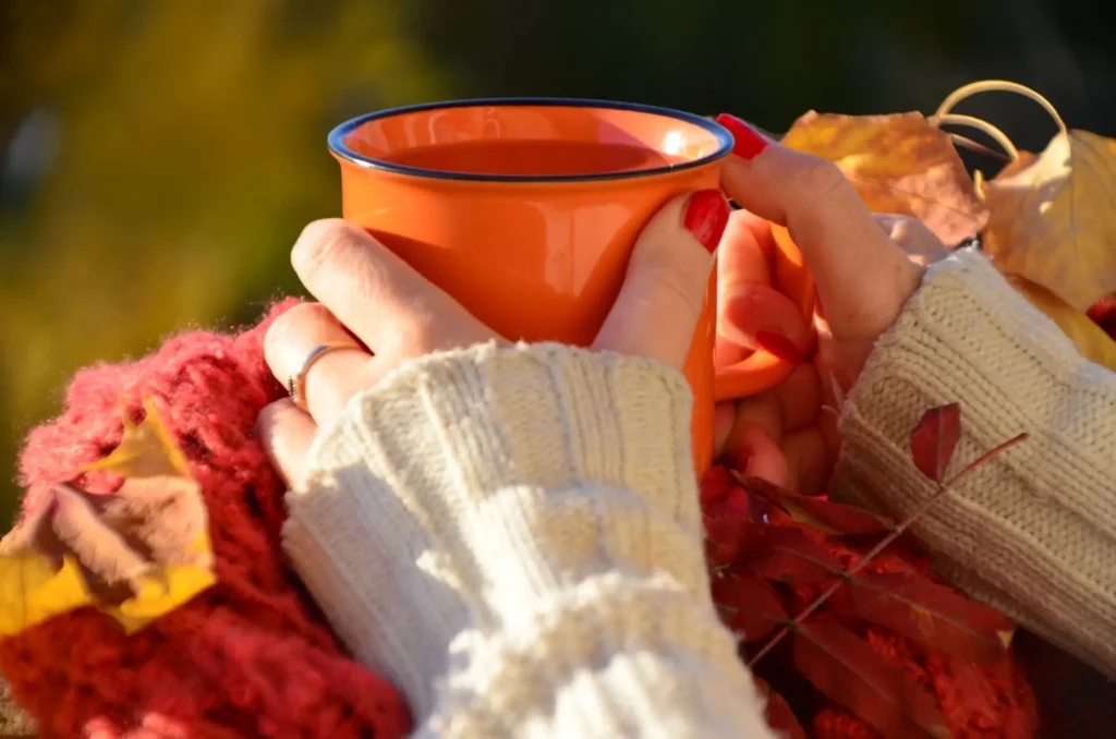 Žena venku drží v rukou oranžový hrnek