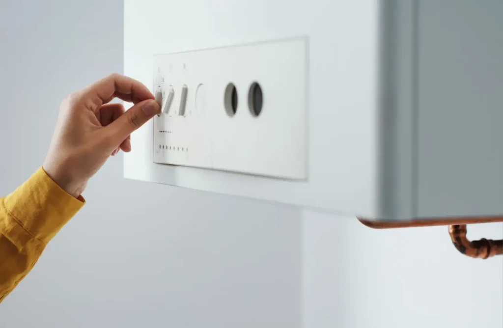 Detail ruky, která otáčí ovladačem starého kotle a nastavuje teplotu vytápění