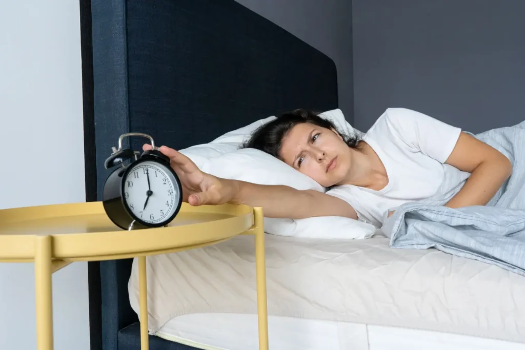 Unavená žena natahuje ruku po budíku a s nechutí začíná den