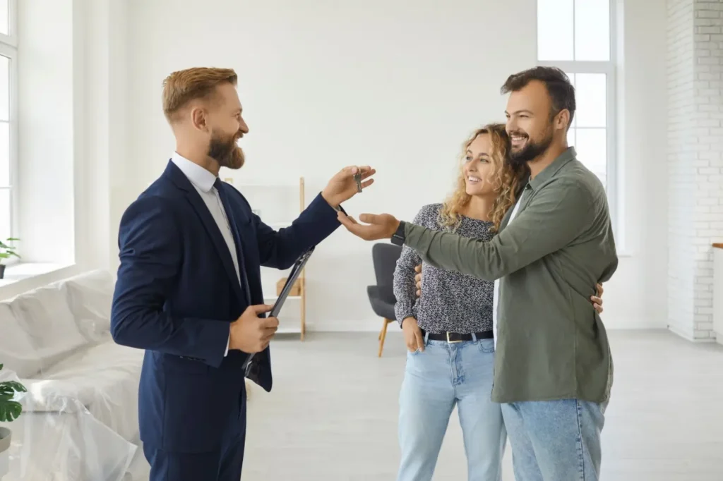 Usměvavý pár přebírá klíče od bytu od realitního makléře v moderním interiéru