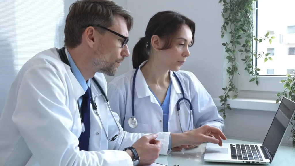 L&eacute;kaři konzultuj&iacute; v&yacute;sledky u poč&iacute;tače v nemocničn&iacute;m prostřed&iacute;