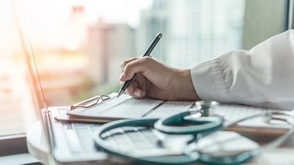 L&eacute;kař zapisuje &uacute;daje do formul&aacute;ře vedle stetoskopu