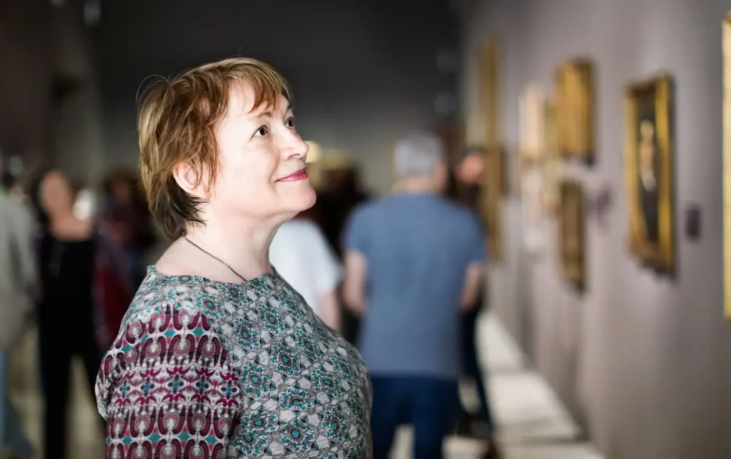 Seniorka s &uacute;směvem sleduje obrazy v galerii