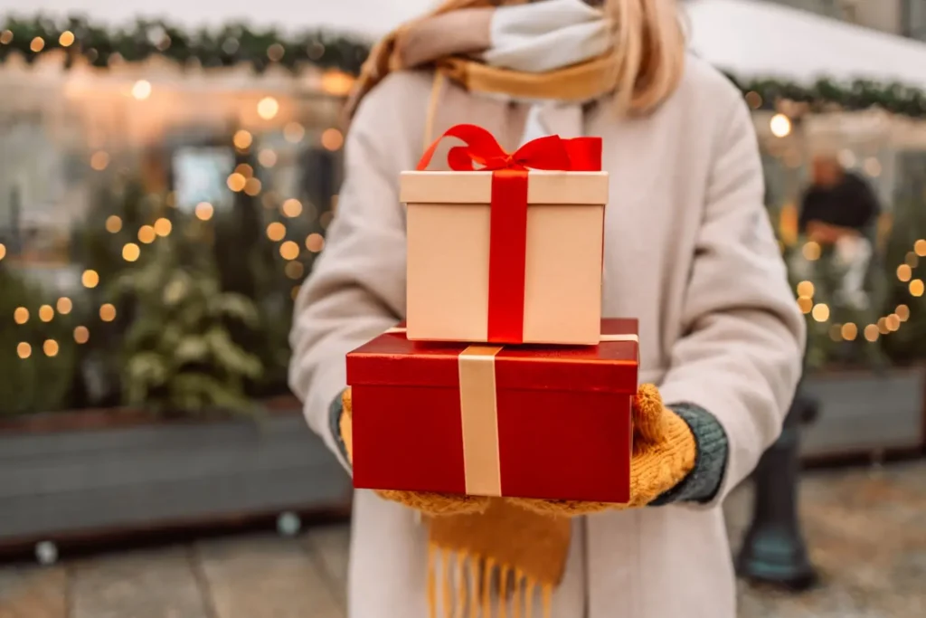 Žena v zimním kabátu drží dvě dárkové krabičky s mašlí