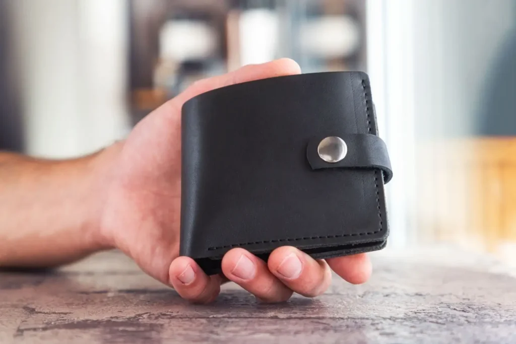 Mužsk&aacute; ruka drž&iacute; černou koženou peněženku