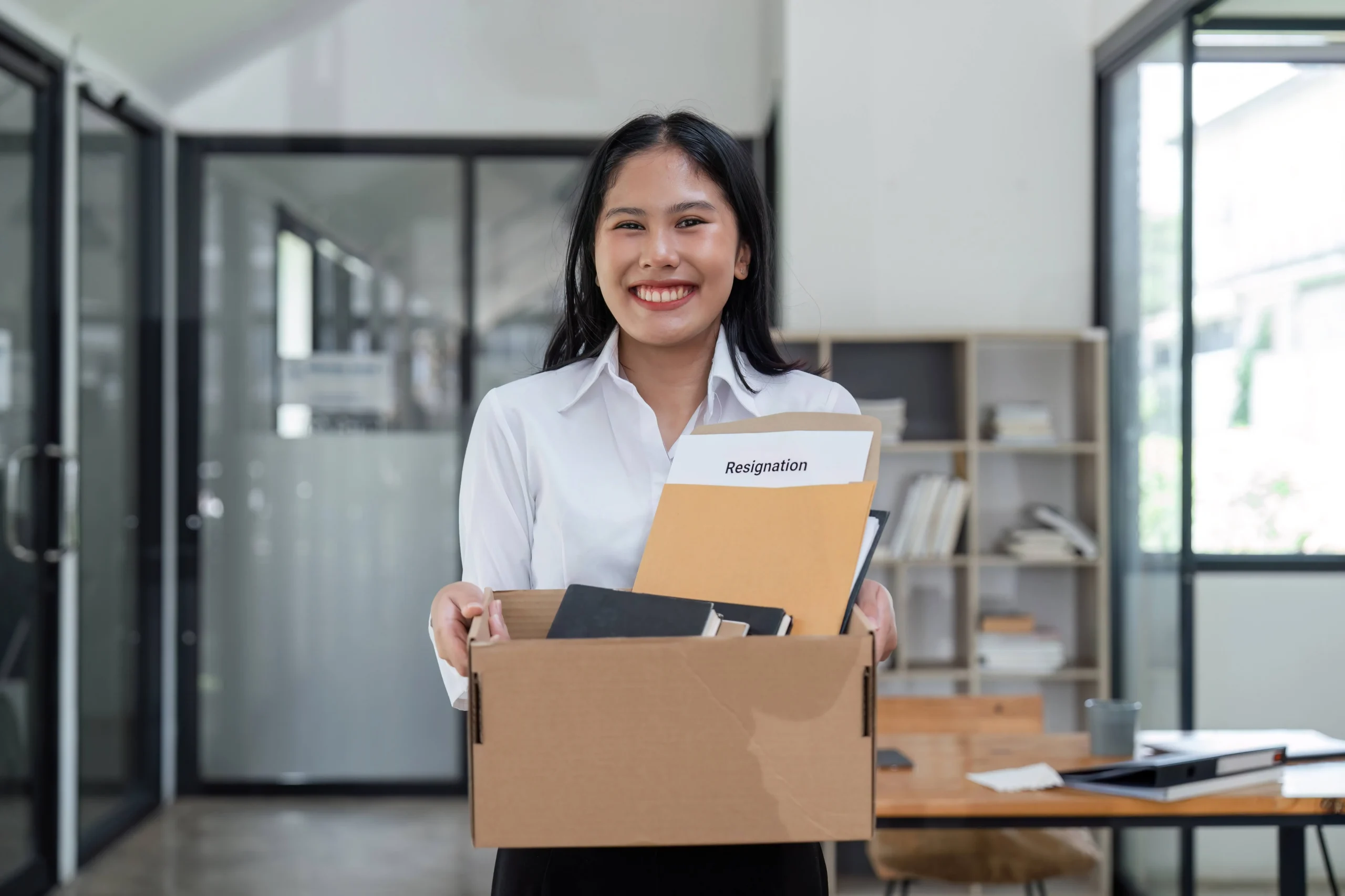 Mlad&aacute; žena si nese s &uacute;směvem krabici s věcmi z kancel&aacute;ře