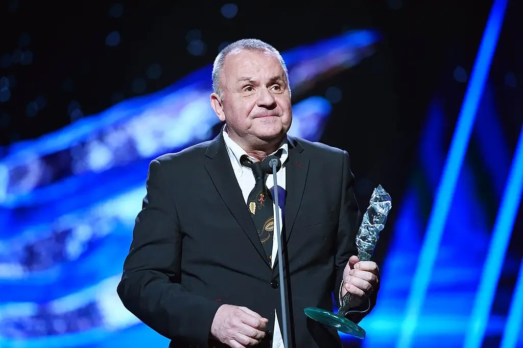 Jožo R&aacute;ž stoj&iacute; na p&oacute;diu v obřadn&iacute;m s&aacute;le a drž&iacute; v rukou skleněnou cenu za hudebn&iacute; př&iacute;nos