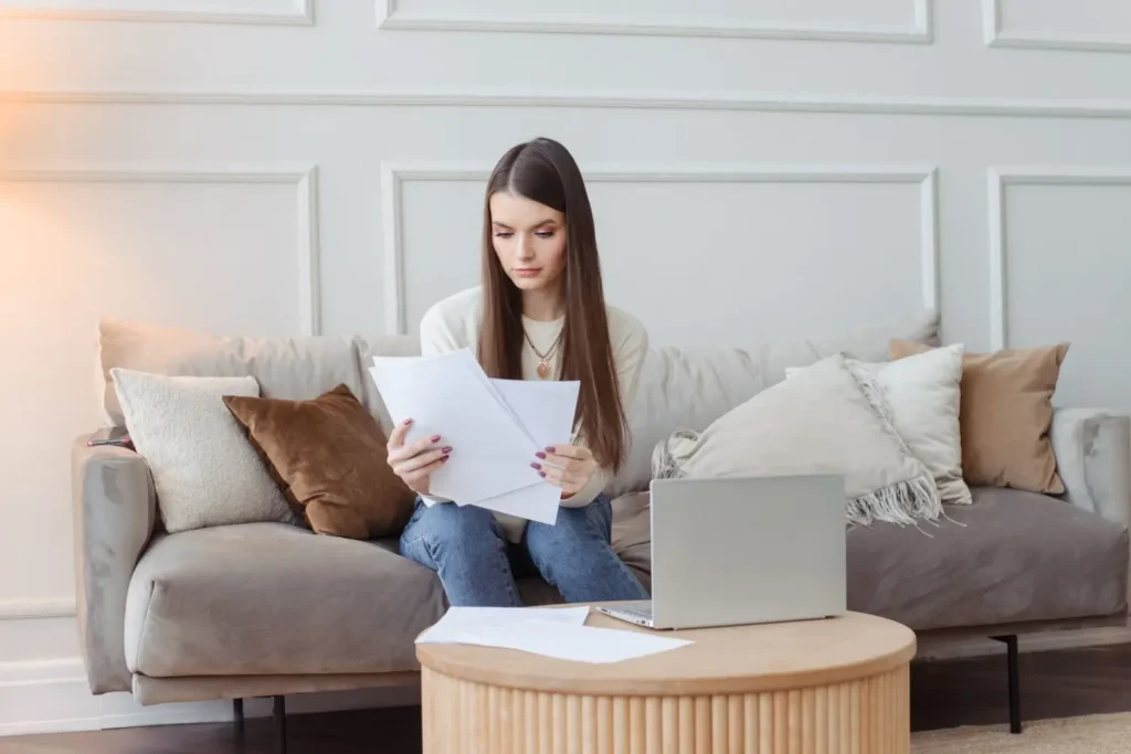 Žena sed&iacute; doma na pohovce a prohl&iacute;ž&iacute; si pap&iacute;ry