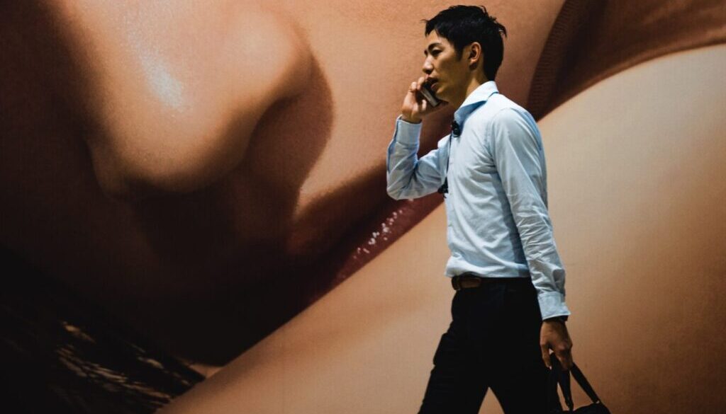man walking while holding smartphone near woman-themed wall painting
