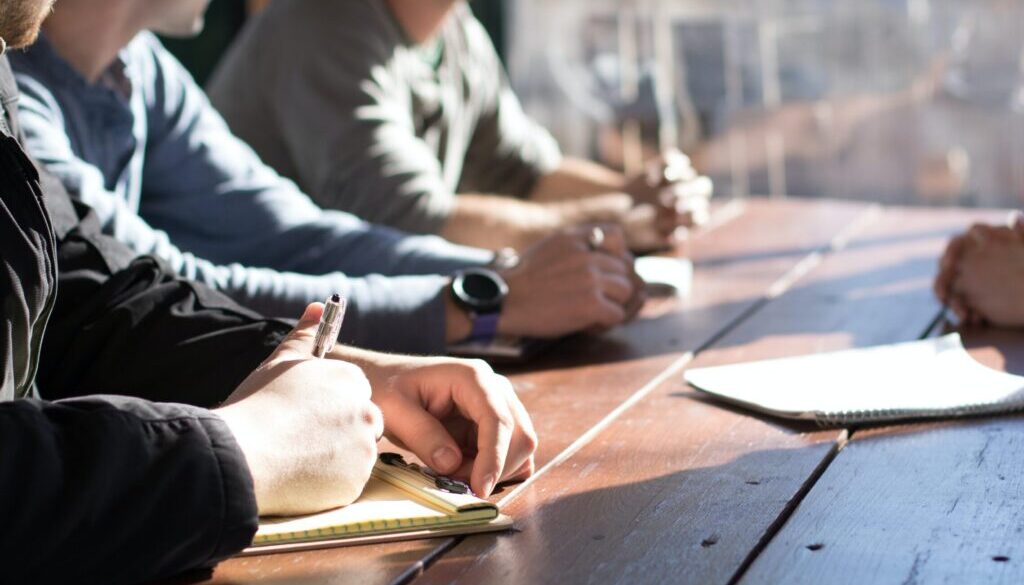 people sitting on chair in front of table while holding pens during daytime