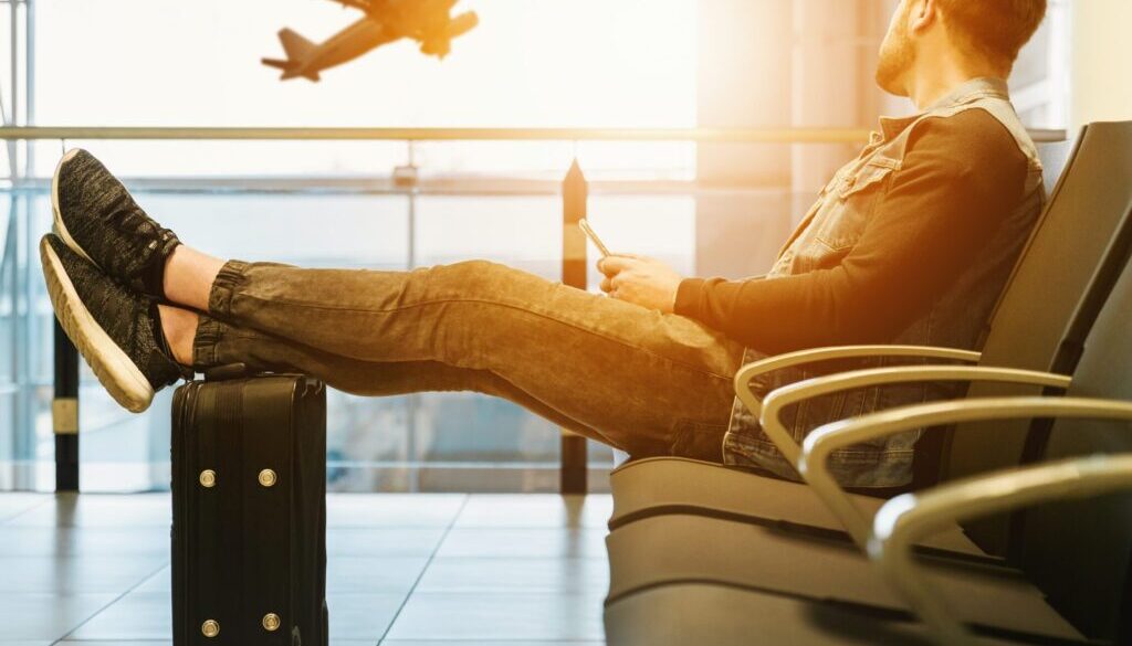 man sitting on gang chair with feet on luggage looking at airplane