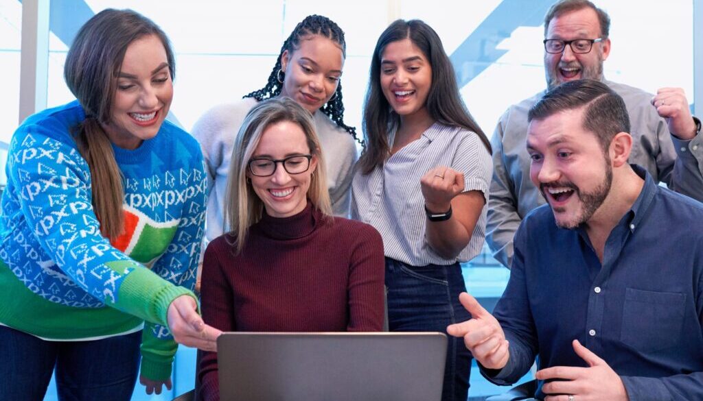men and women sitting and standing while staring at laptop