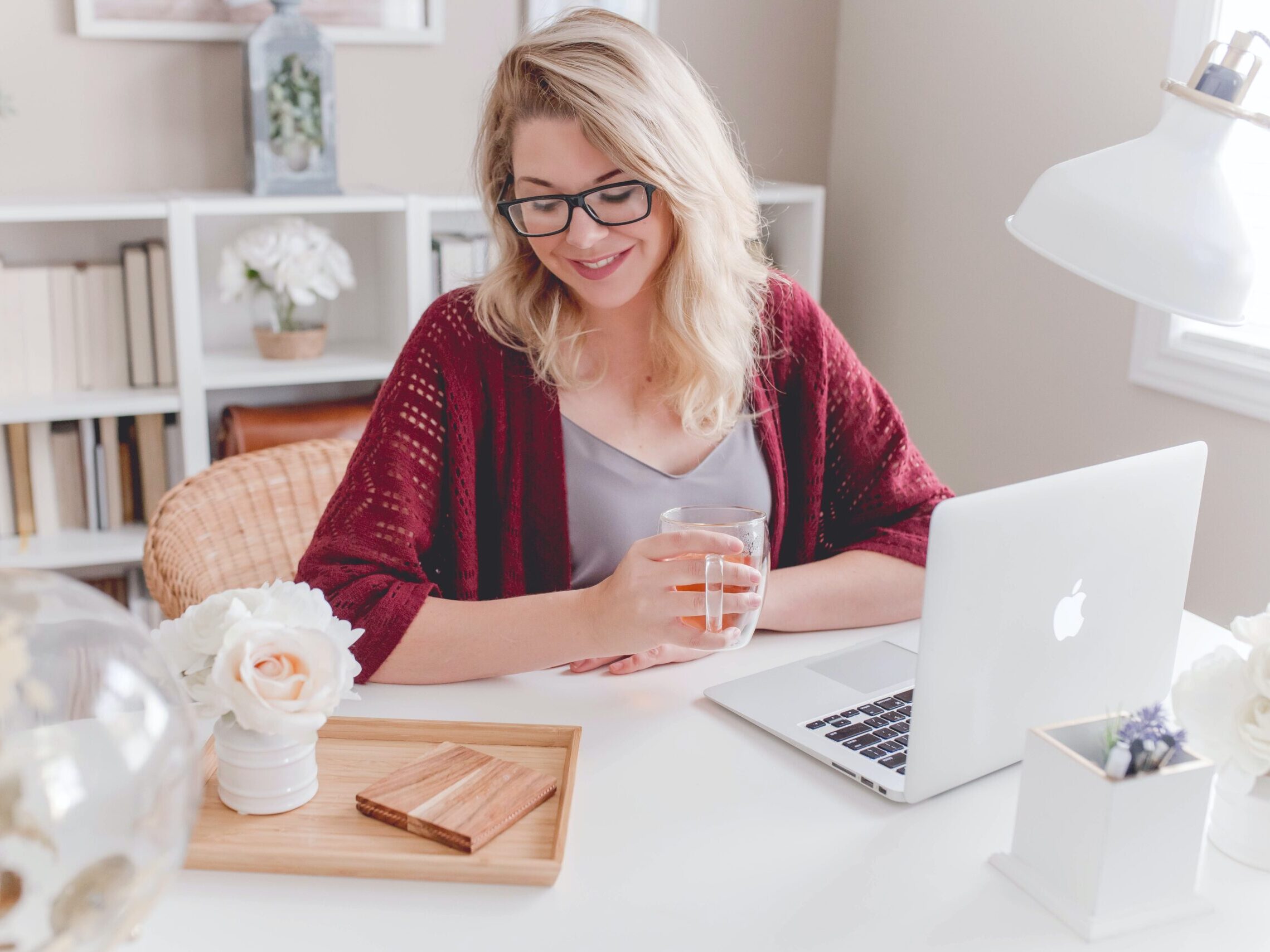 woman smiling holding glass mug sitting beside table with MacBook