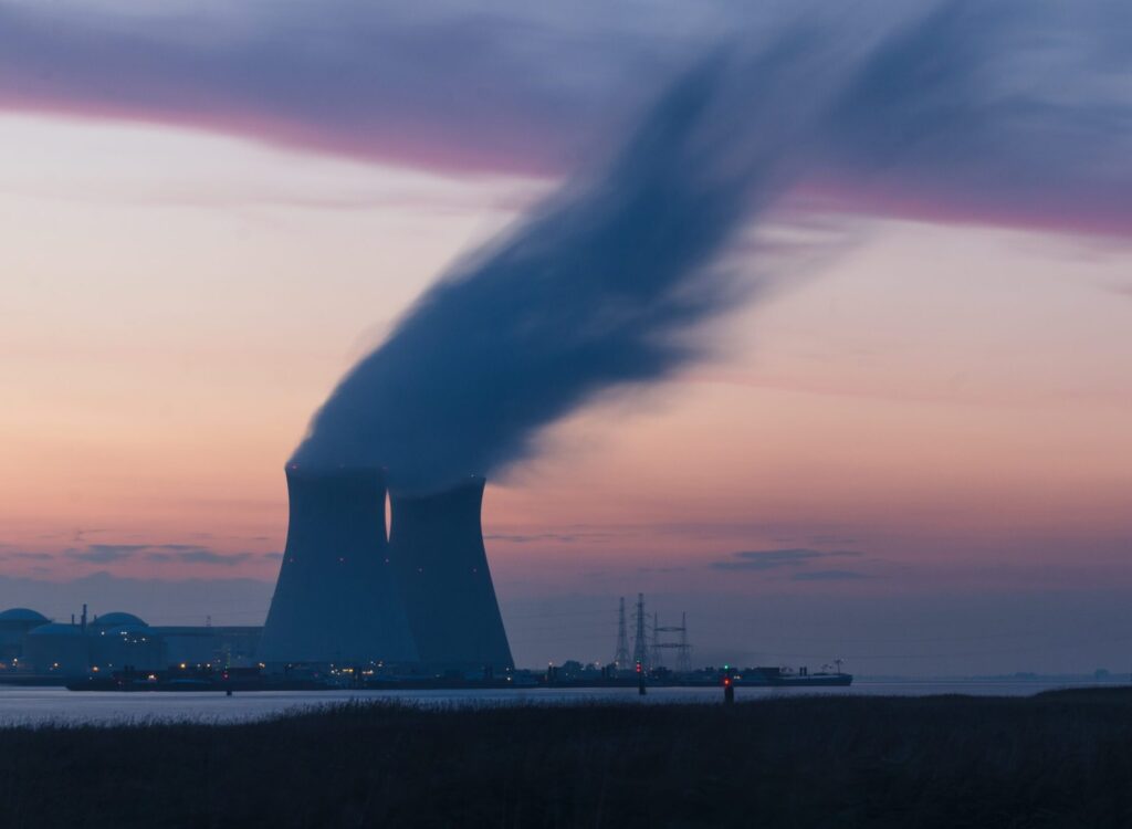 skyline photography of nuclear plant cooling tower blowing smokes under white and orange sky at daytime